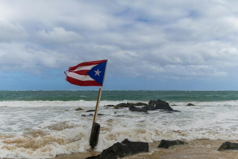 A Puerto Rican flag waves on a rocky beach under a cloudy sky, capturing a sense of national pride.