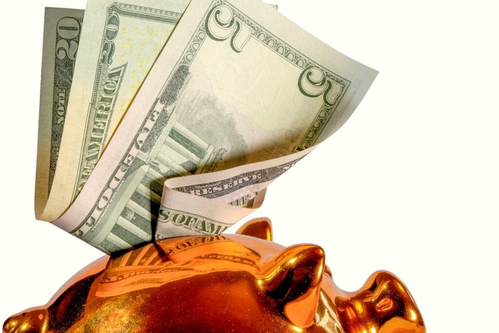 Us dollar bills being inserted into a piggy bank